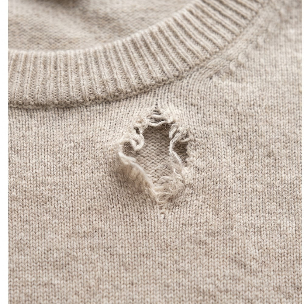 A torn hole near the neckline of a beige knit sweater