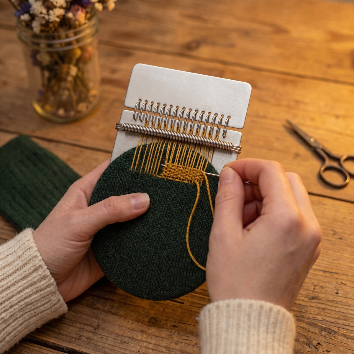 Hands darning the heel of a green wool sock on the LAGA loom