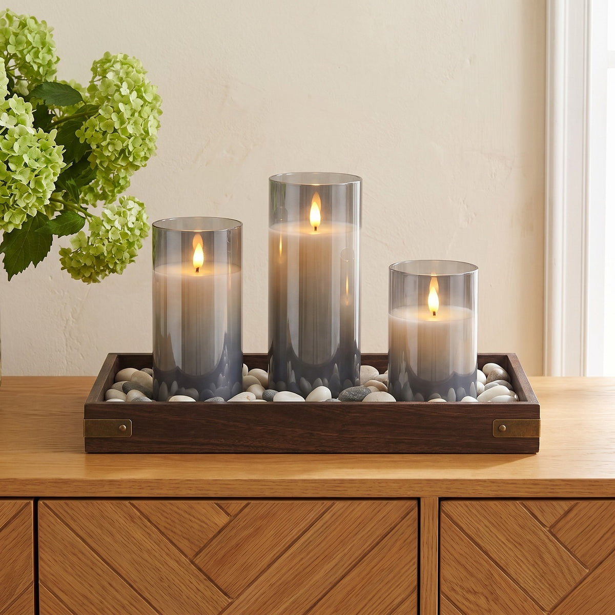 Gray VEKE candles in a wooden pebble tray on an oak sideboard