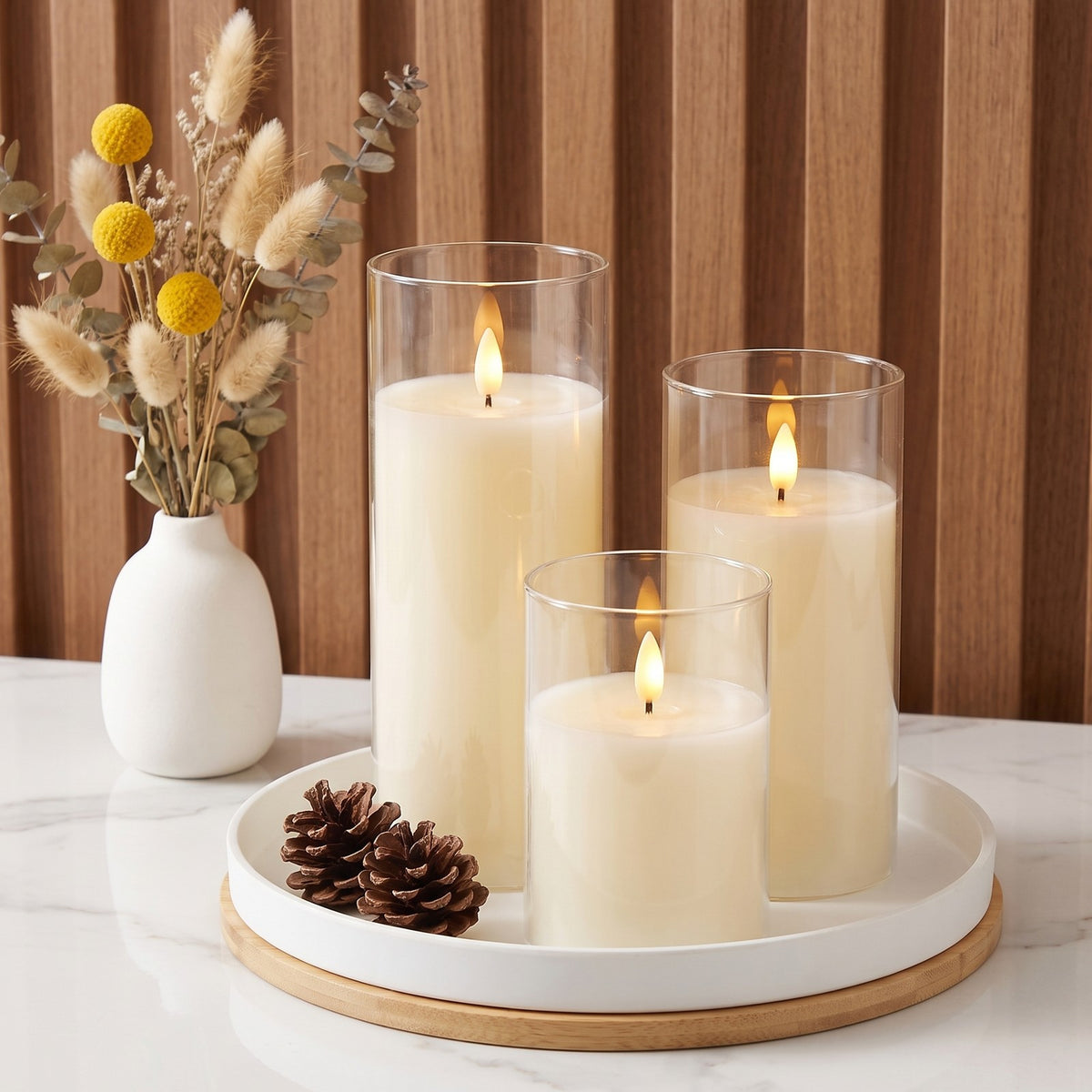 Clear VEKE candles on a round white tray with pinecones and dried flowers