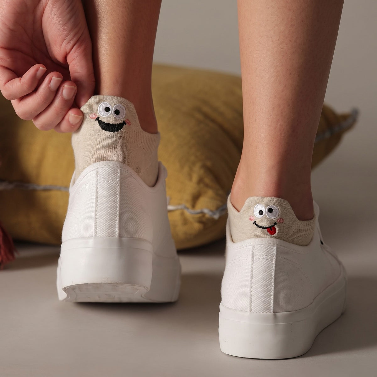 Pulling up the heel tab of a cream TASSA sock in white sneakers