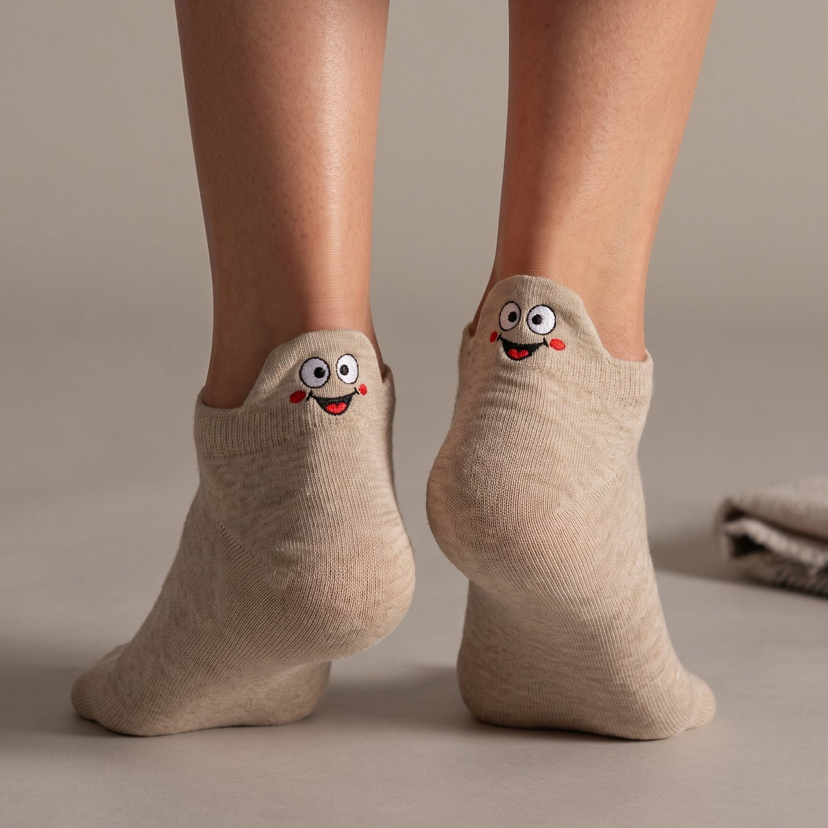 Oatmeal TASSA socks with rosy-cheeked faces on the heel tabs