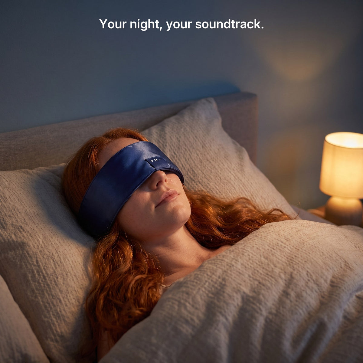 A woman asleep at night wearing the navy satin Hushband over her eyes