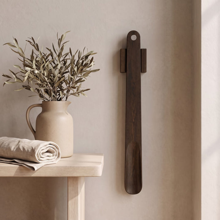Walnut — KLIVA magnetic shoehorn hanging on a plaster wall beside a small side table