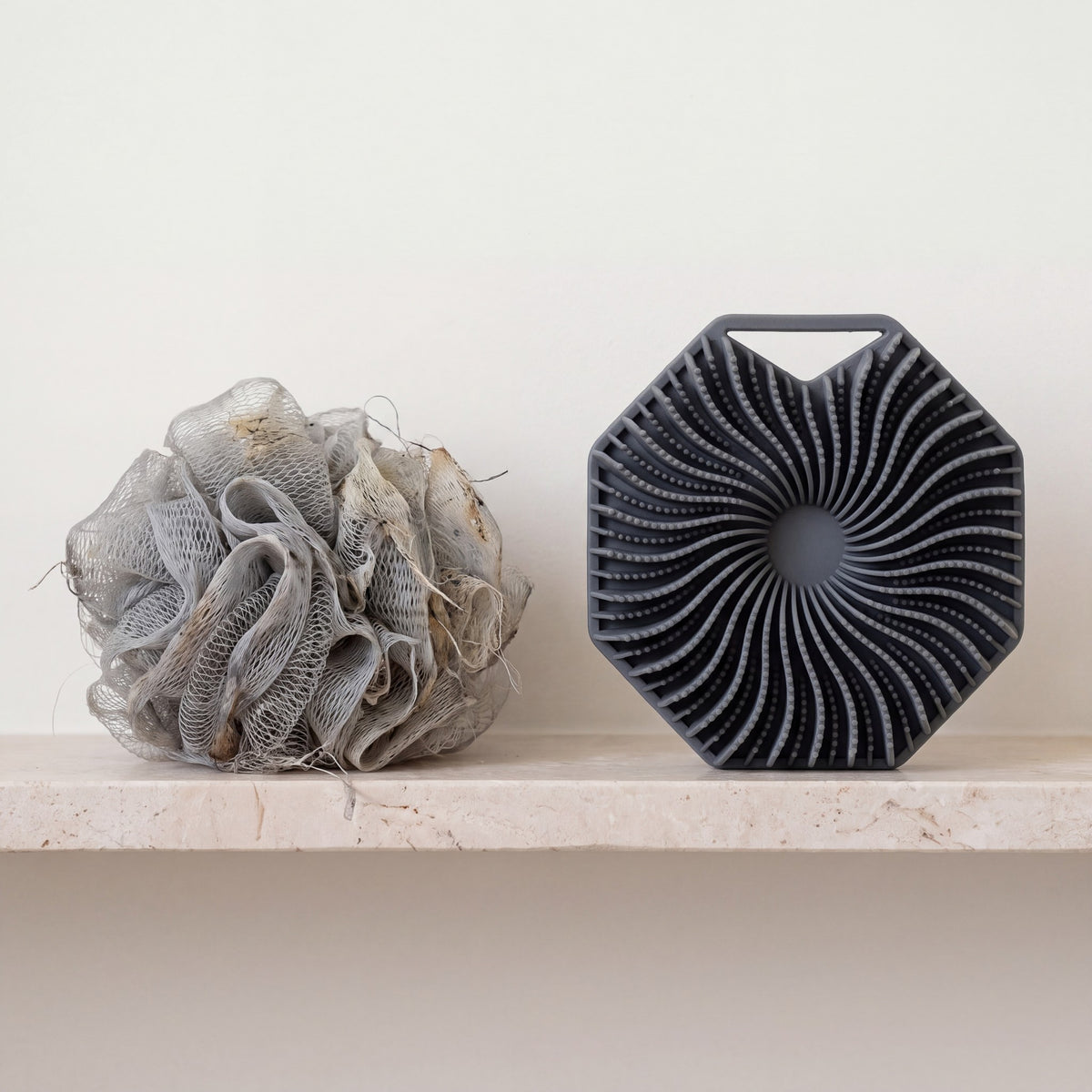A worn mesh shower pouf next to a clean SKURA scrubber
